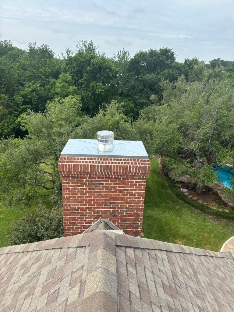 Silver metal chimney cap on a red brick chimney surrounded by trees